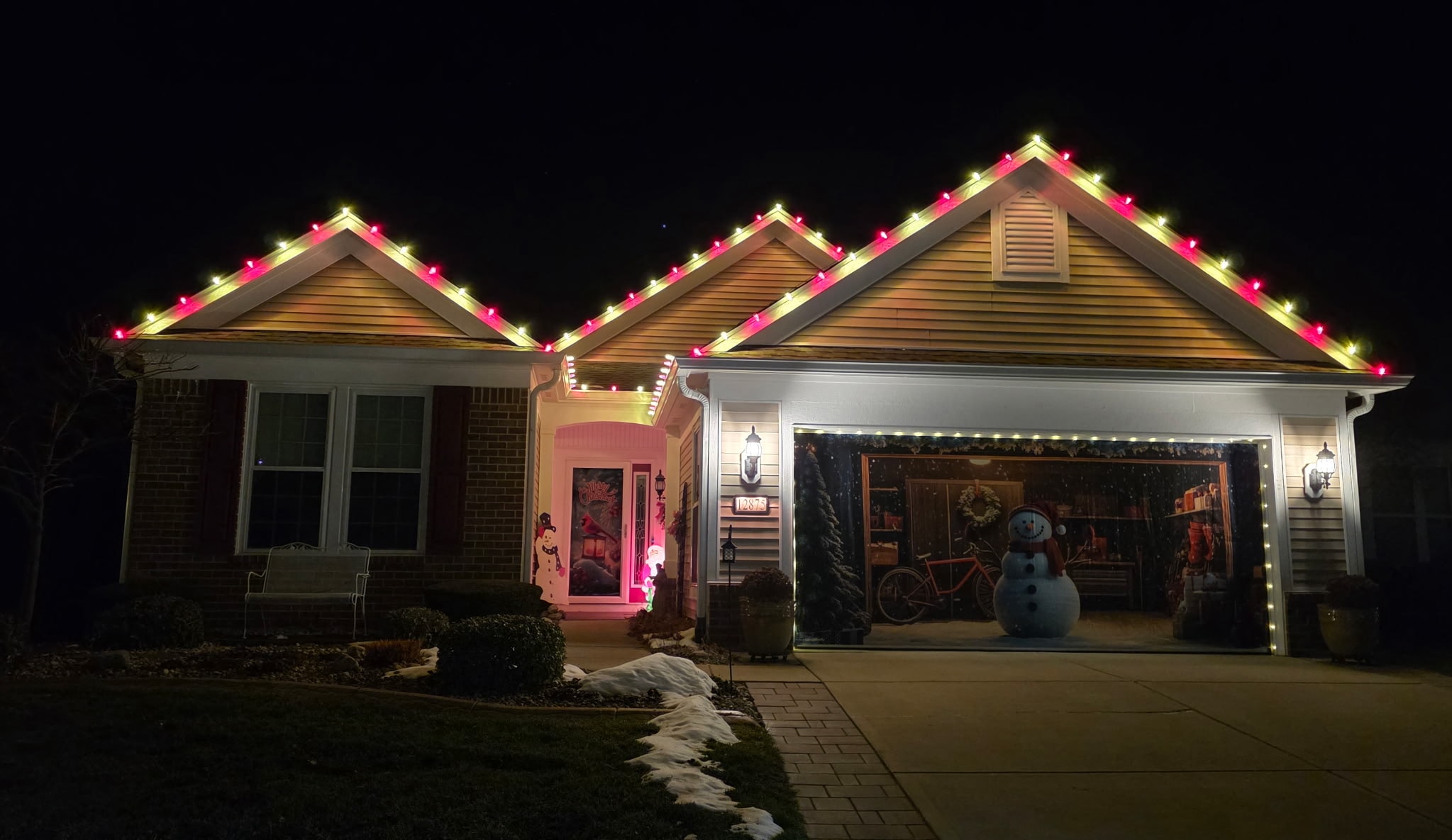 Home decorated with colorful Christmas roofline lights and snowman display at night
