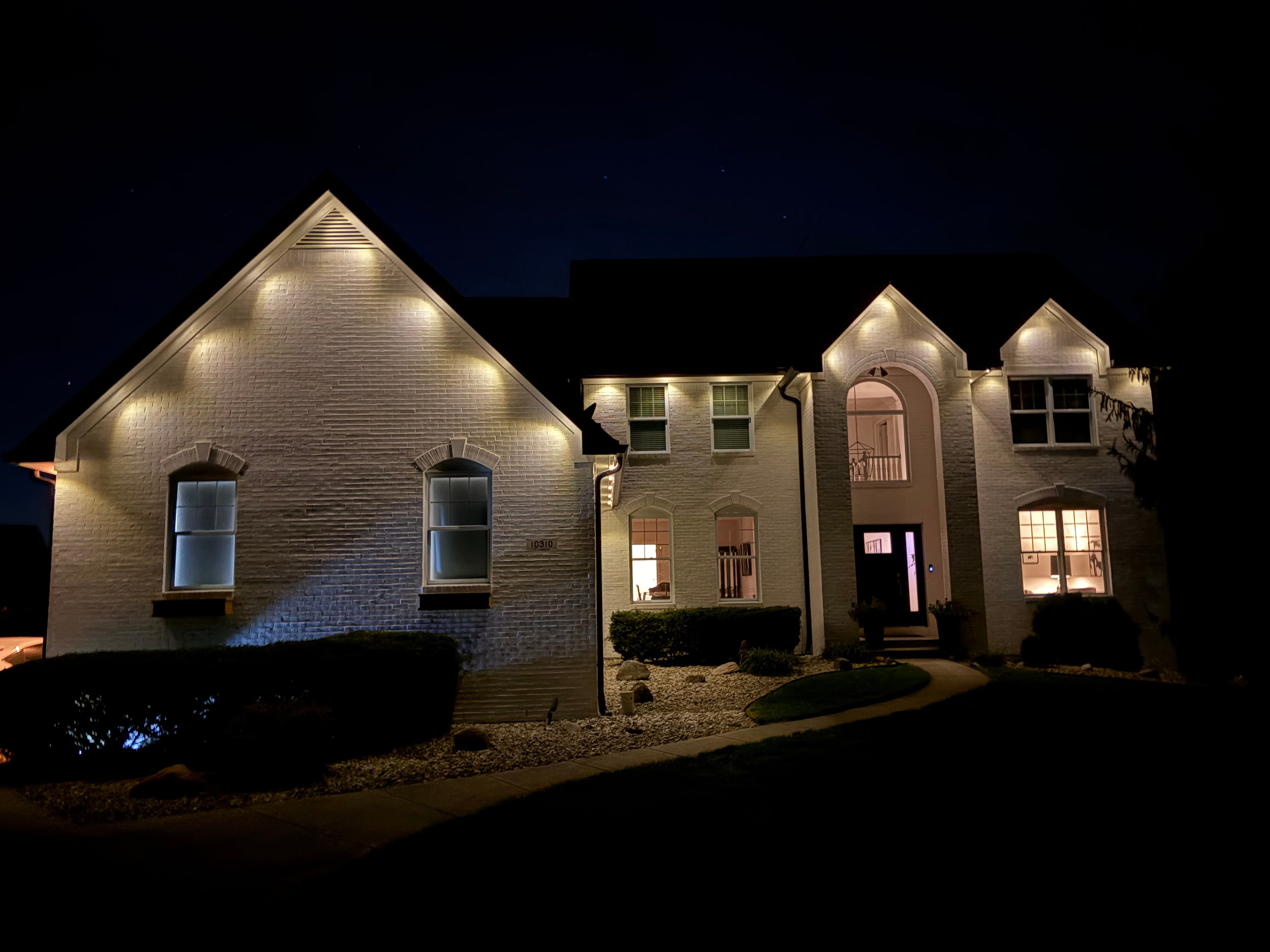 Large brick home with warm white permanent LED roofline uplighting at night